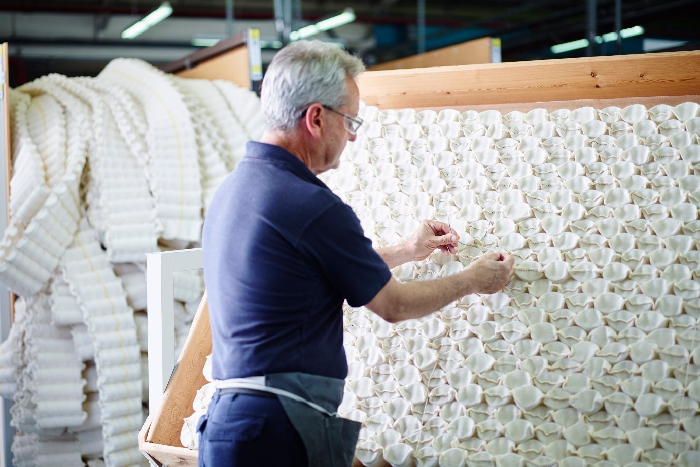 Vispring mattress Plymouth factory scene - mature man meticulously threading needle and tufting mattress springs 